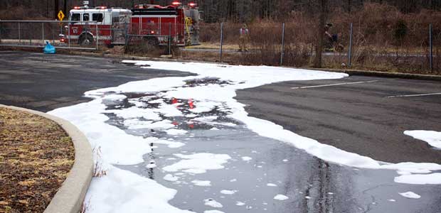 water and firefighting foam on a road with a fire engine behind a fence